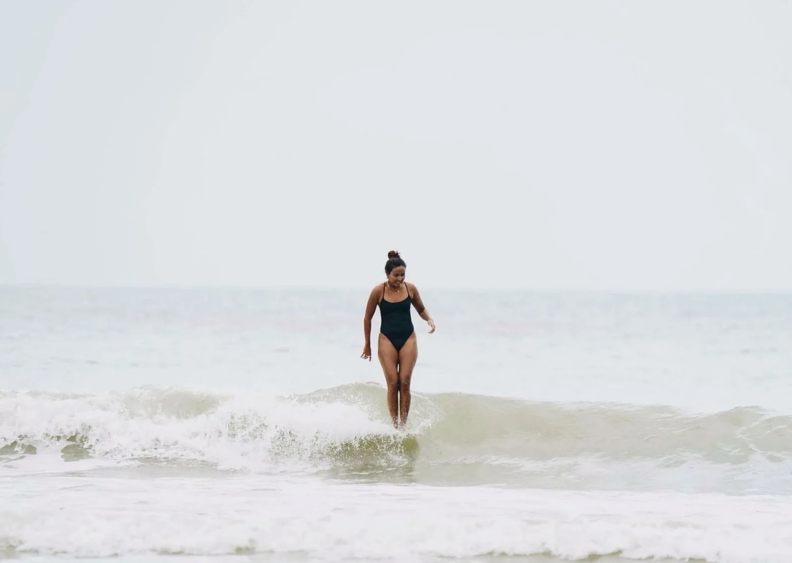 Swimmer in a black one-piece walking out of a small wave on a pale beach
