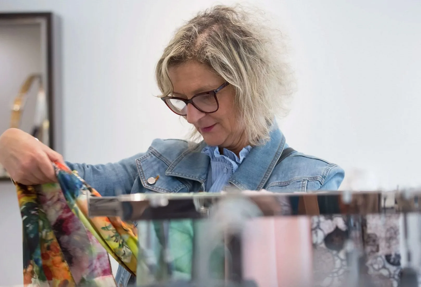 Woman in a denim jacket sorting colourful scarves in a shop