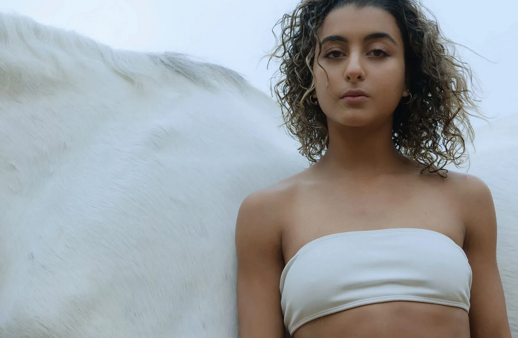 Woman in a white bandeau top in front of a white feathered backdrop