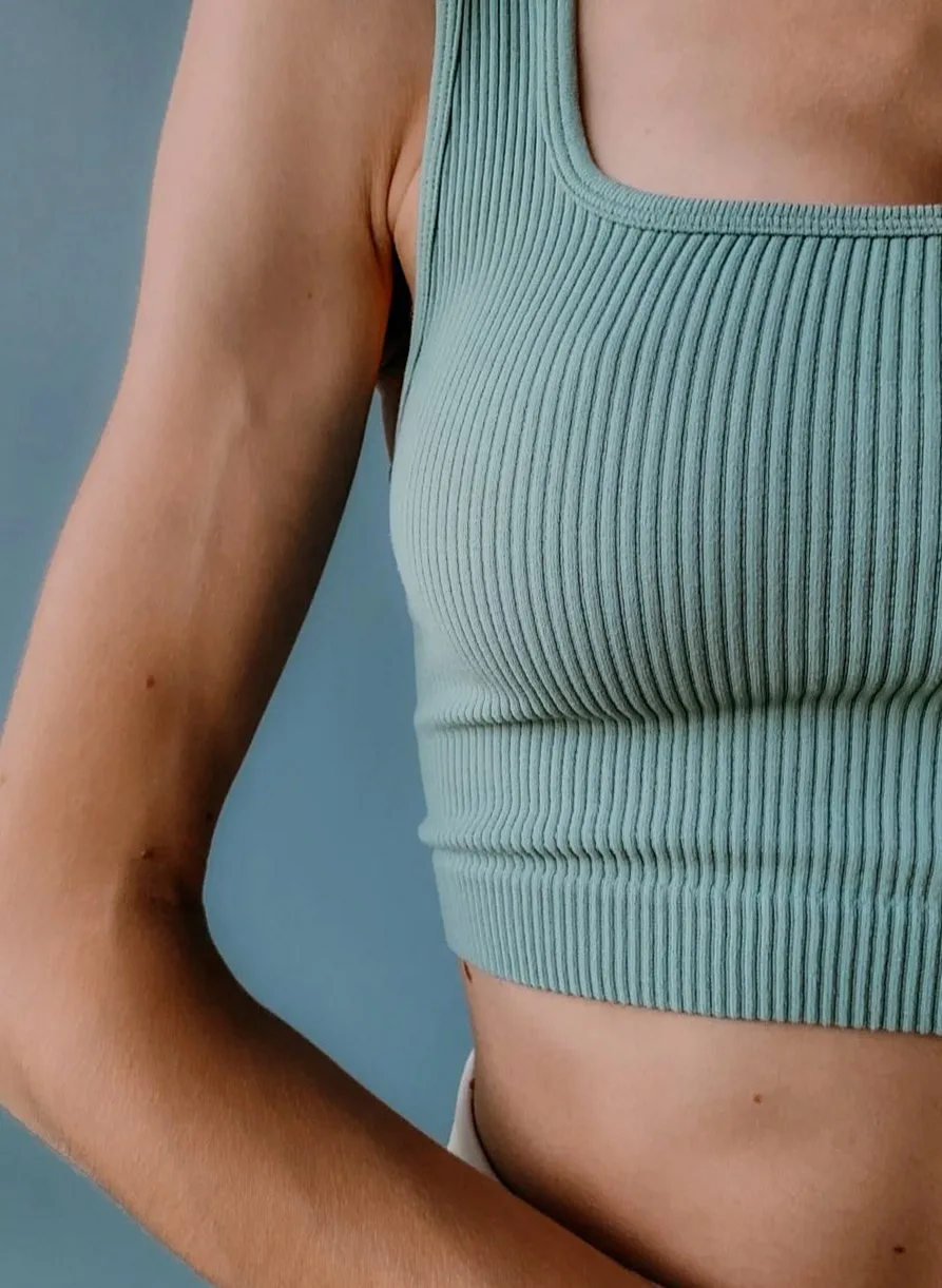 Close-up of a sage-green ribbed swim top on a woman standing against a blue-grey wall